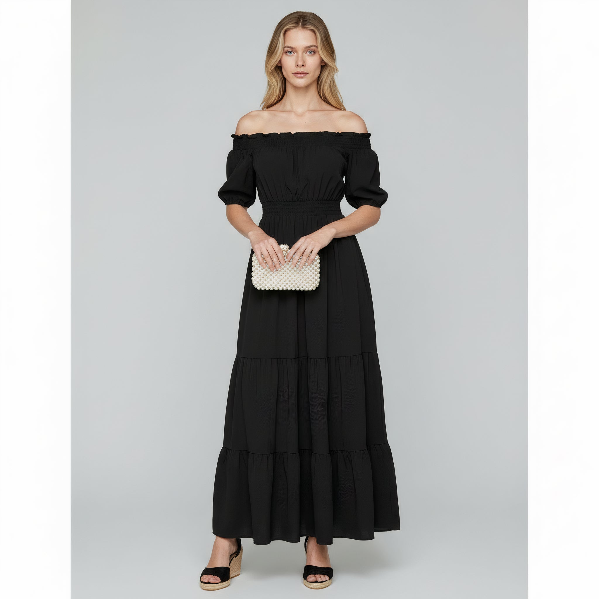 woman wearing black off shoulder maxi dress on a plain background